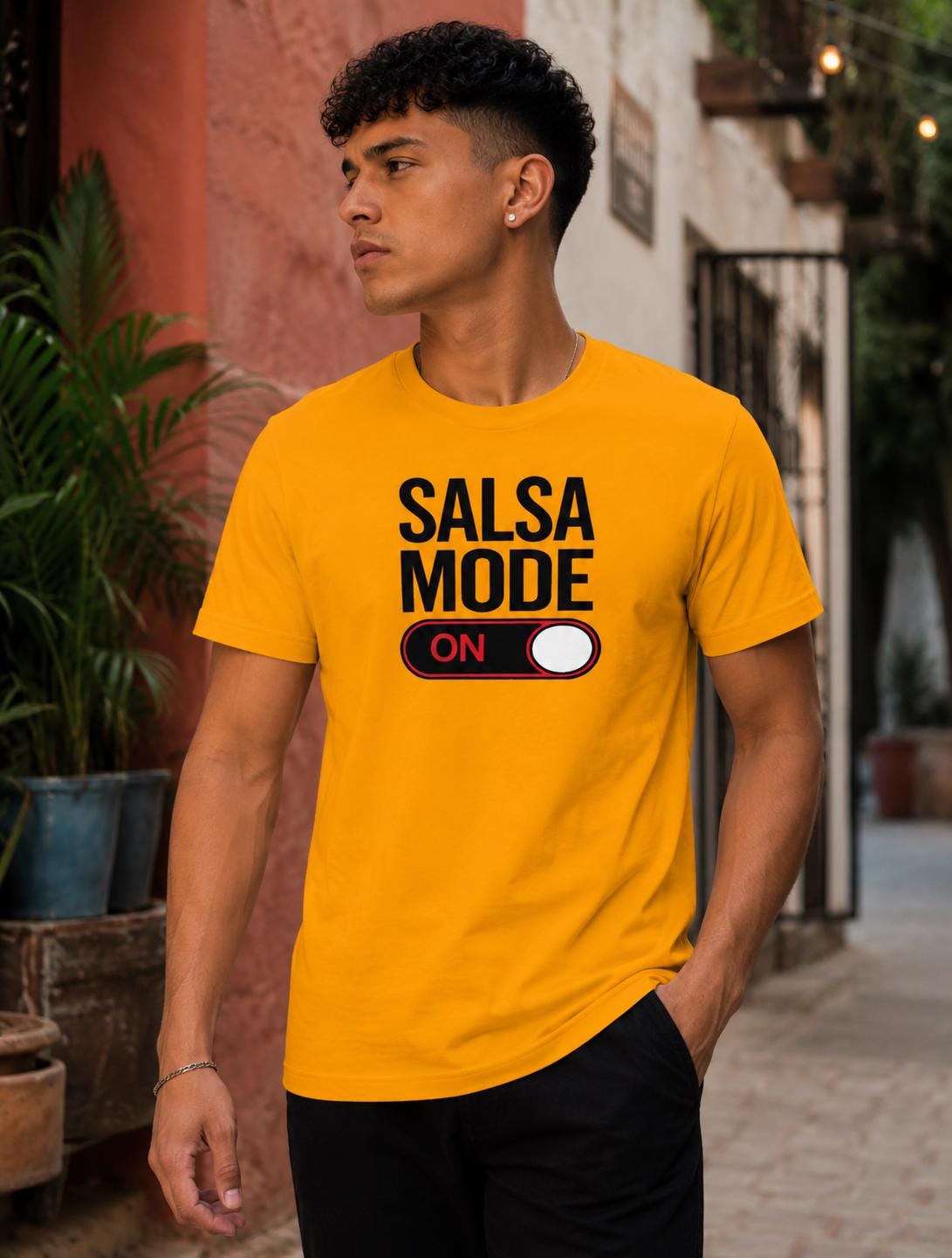 Male model wearing a bright yellow “Salsa Mode ON” graphic t-shirt with bold black lettering and switch design, styled casually in an outdoor street setting. Fun salsa dance apparel for Latin dance lovers, social dancers, and salsa lifestyle fashion.