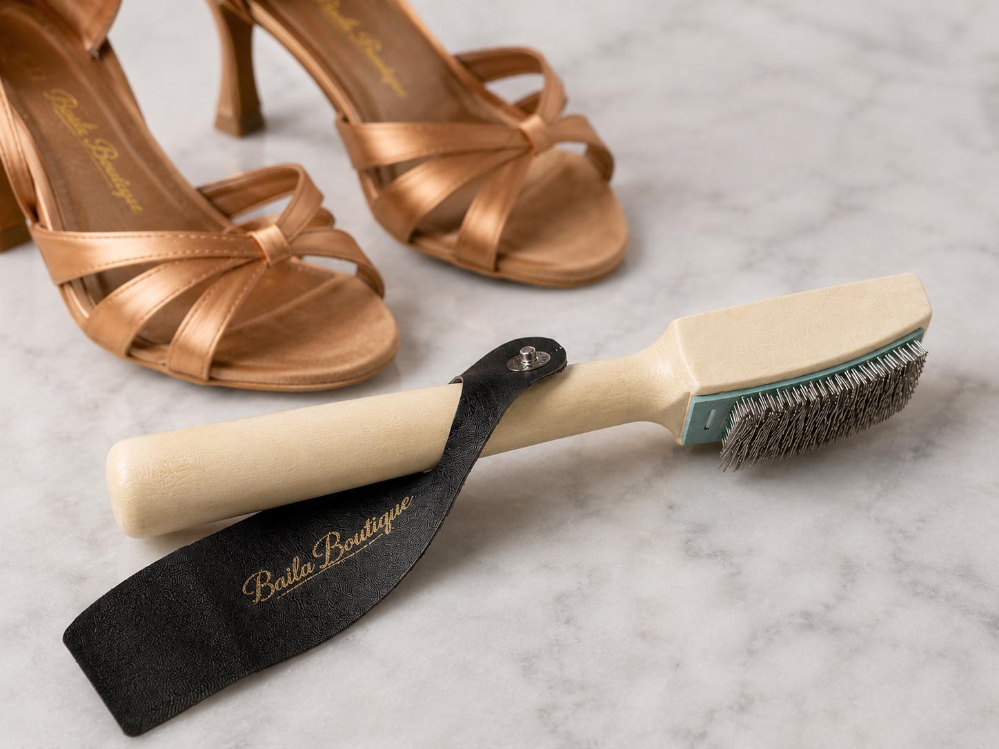 Baila Boutique dance shoe brush with wooden handle and metal bristles designed for cleaning suede salsa and bachata dance shoes. Professional Latin dance shoe accessory with black protective cover for dancers and social dance events.