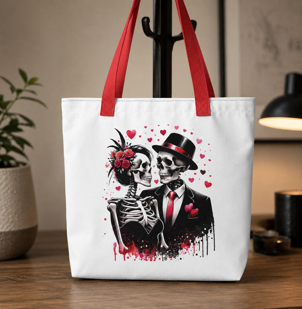 White tote bag with red handles featuring a romantic gothic skeleton couple design with roses, hearts, and elegant black-and-red formal attire. Stylish alternative fashion accessory perfect for gothic lovers, Halloween style, everyday shopping, and dark aesthetic gifts.