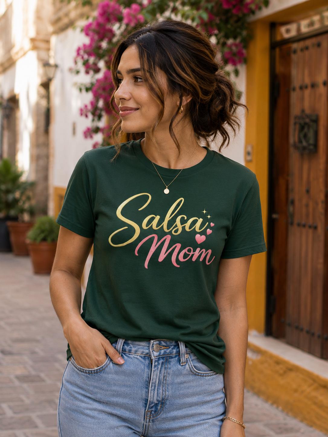 Woman wearing a dark green “Salsa Mom” graphic t-shirt with gold and pink lettering, styled casually with blue jeans in a warm outdoor street setting. Perfect Latin dance apparel gift for salsa lovers and dance moms.